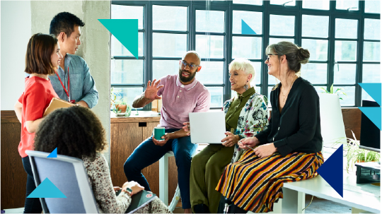 A group of people sit around each other in an office setting and talk in what looks like a meeting.