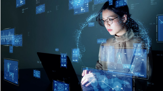 A woman works in a laptop as she is surrounded by several blue interfaces. She is wearing glasses, a beige blouse and pink lipstick.