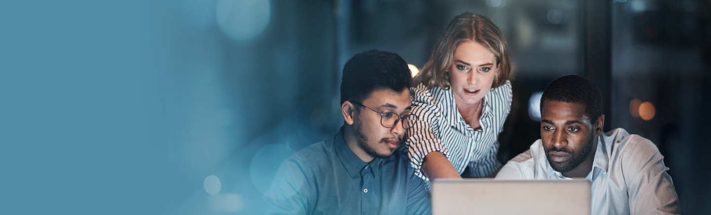 Two men and a woman look at a computer in front of them. The woman is pointing and she is wearing a striped shirt.